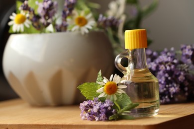 Bottle of natural lavender essential oil near mortar with flowers on wooden table, closeup. Space for text