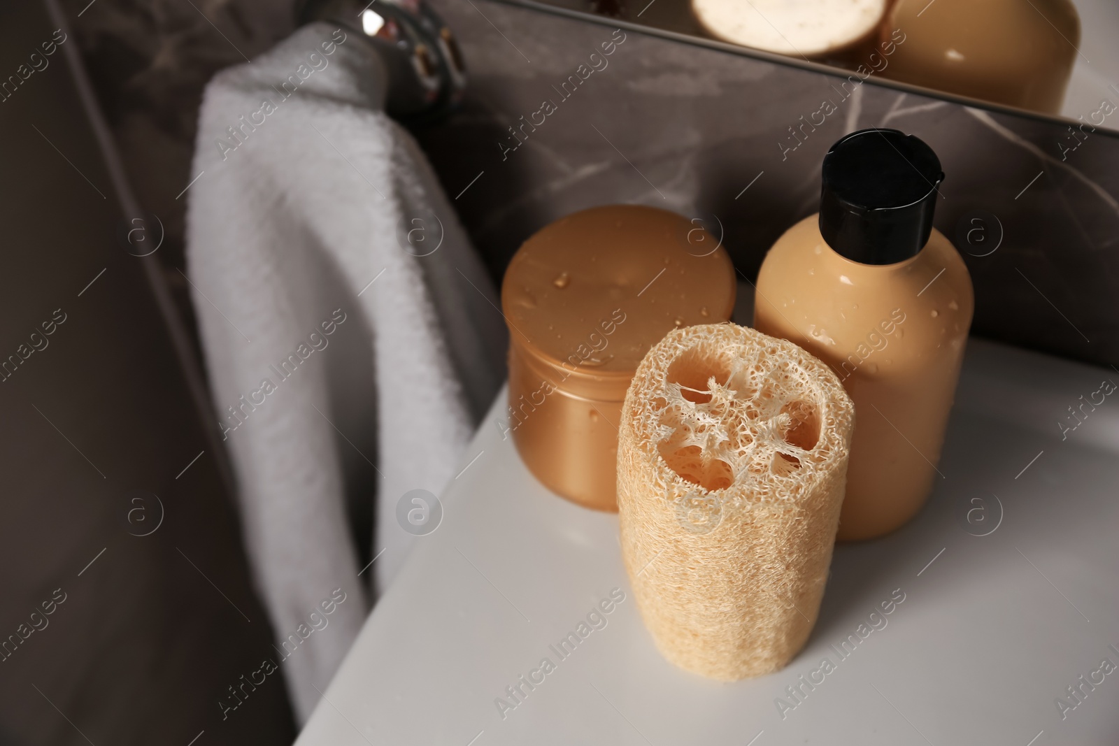 Photo of Natural loofah sponge and cosmetic products on washbasin in bathroom, above view