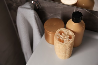 Photo of Natural loofah sponge and cosmetic products on washbasin in bathroom, above view