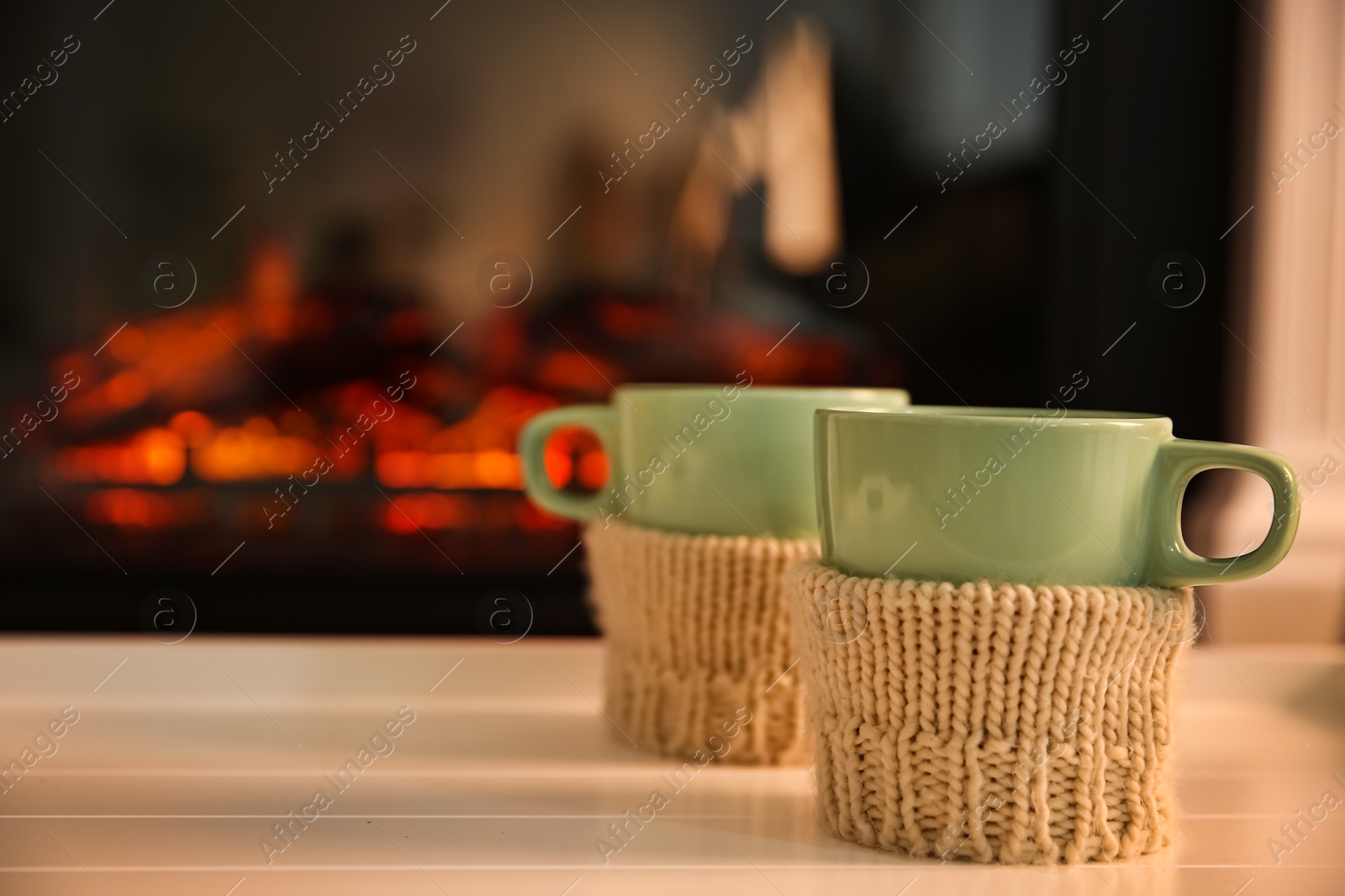 Photo of Cups with hot drink on light table against fireplace, space for text