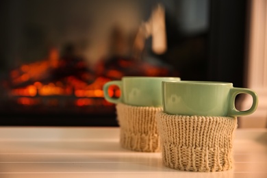 Photo of Cups with hot drink on light table against fireplace, space for text