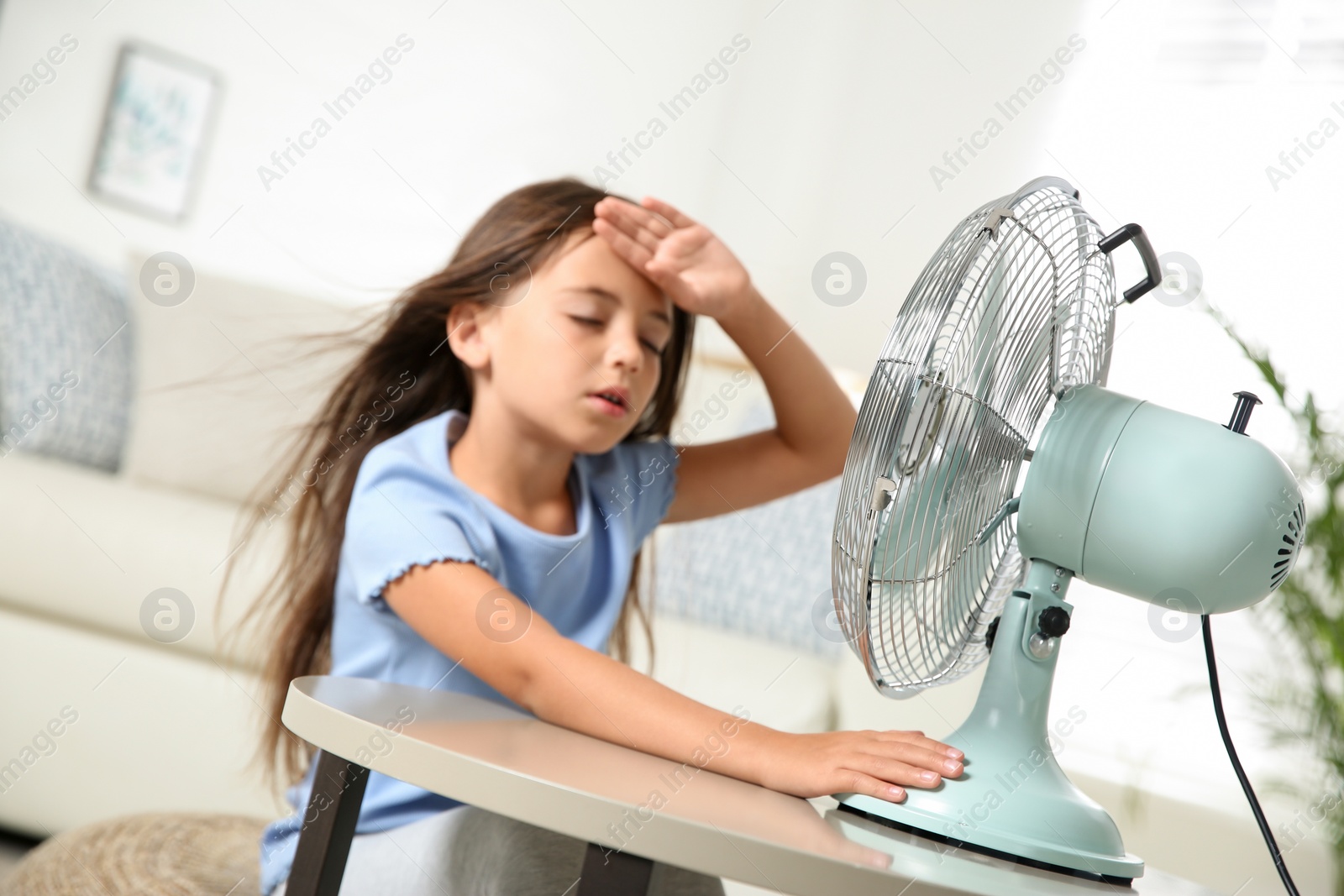 Photo of Little girl suffering from heat in front of fan at home. Summer season