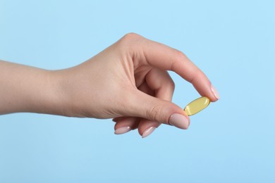 Photo of Woman holding vitamin capsule on light blue background, closeup. Health supplement