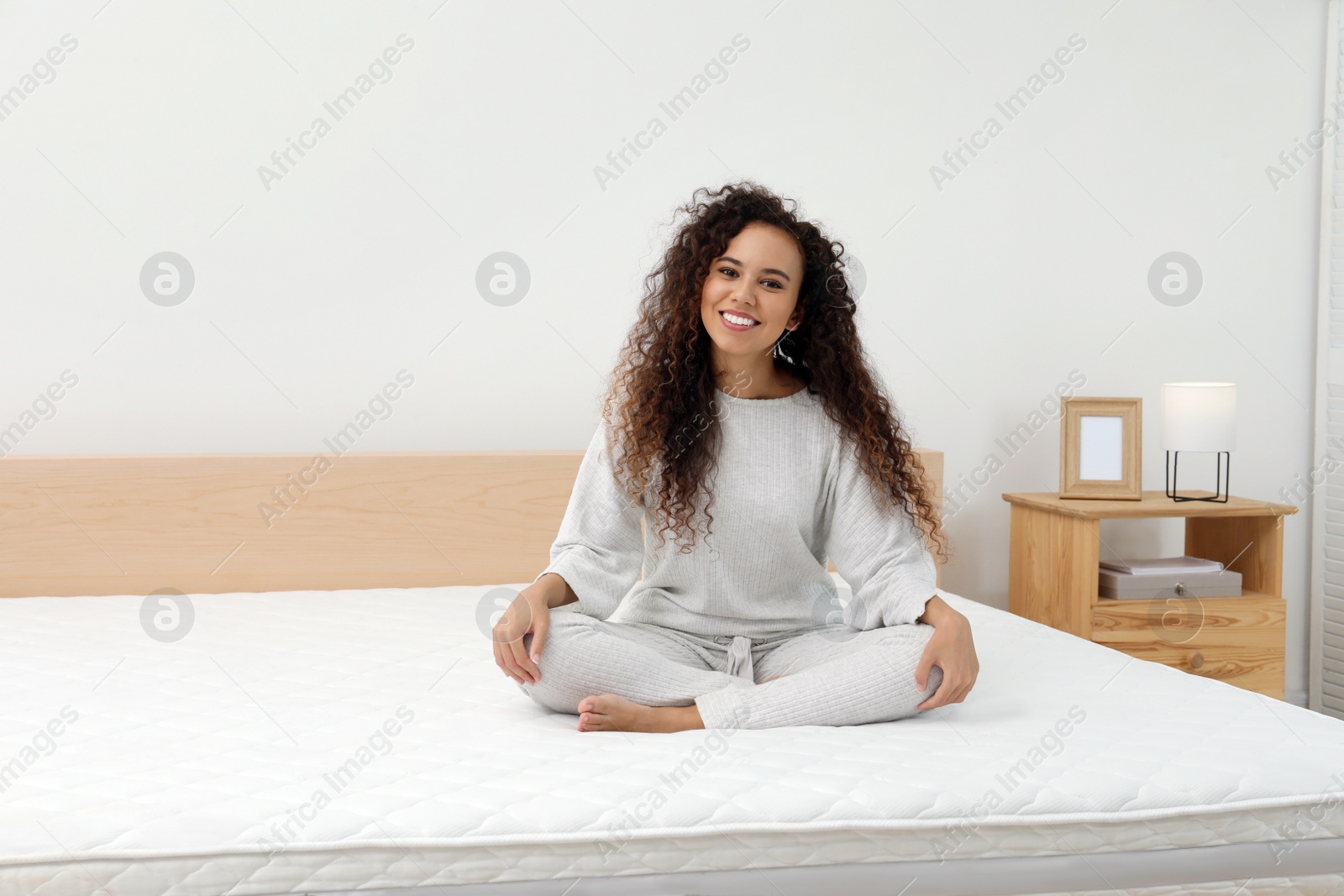 Photo of Happy young African American woman on bed with comfortable mattress at home