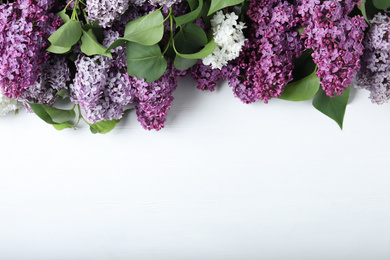 Photo of Different blossoming lilac branches on white wooden background, flat lay. Space for text