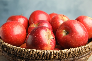 Photo of Wicker bowl with ripe juicy red apples against blue background, closeup