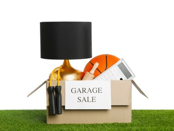 Photo of Different stuff in box with sign Garage Sale on green grass against white background