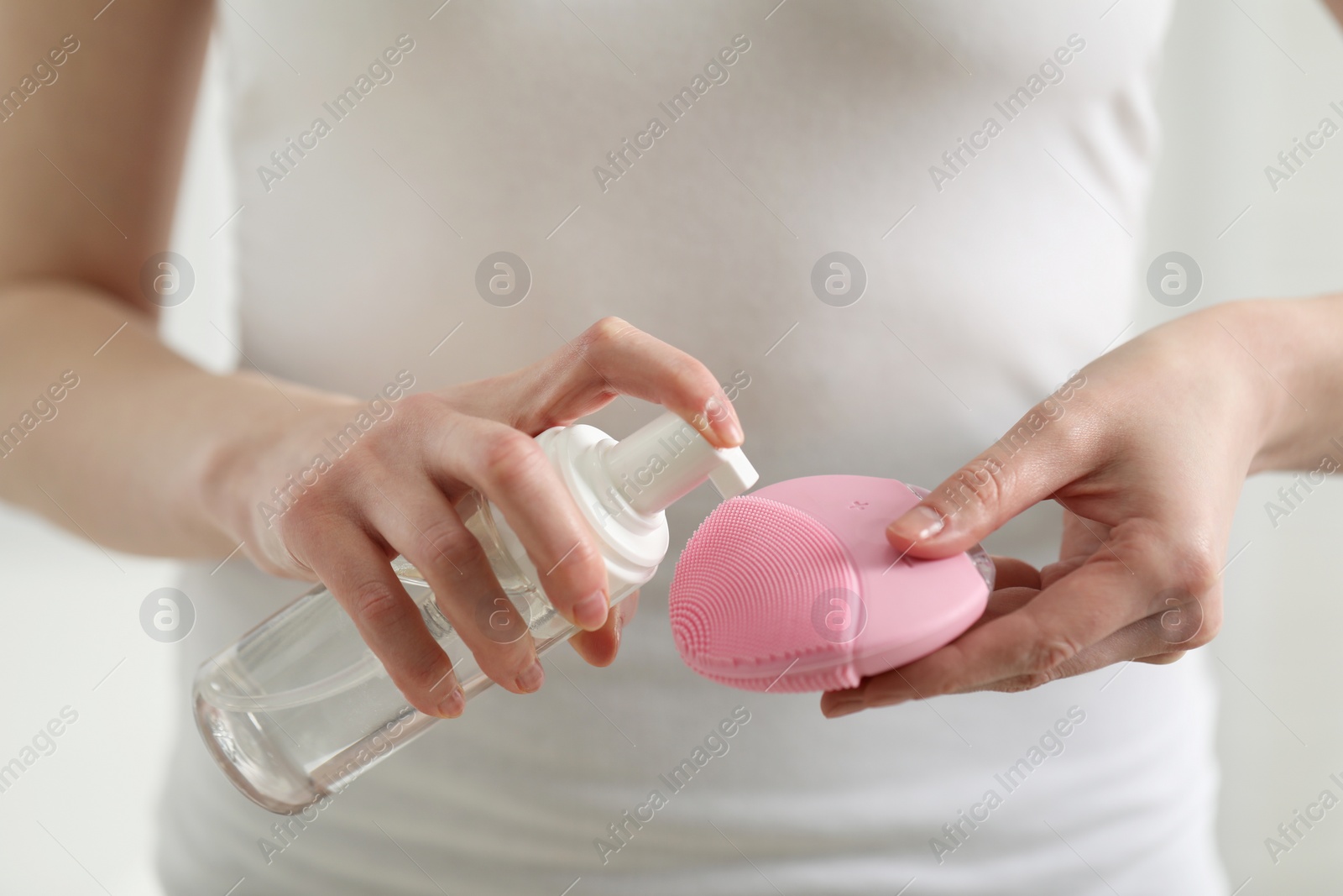 Photo of Washing face. Woman applying cleansing foam onto brush against light background, closeup