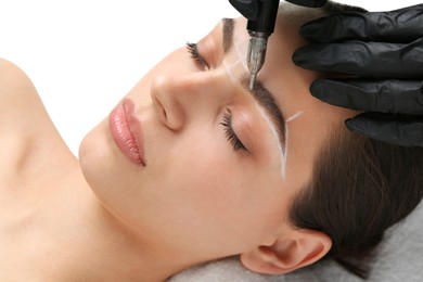 Photo of Beautician making permanent eyebrow makeup to young woman on white background, closeup