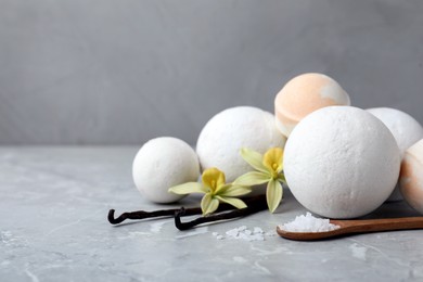 Photo of Fragrant bath bombs, sea salt, vanilla sticks and flowers on grey marble table, space for text