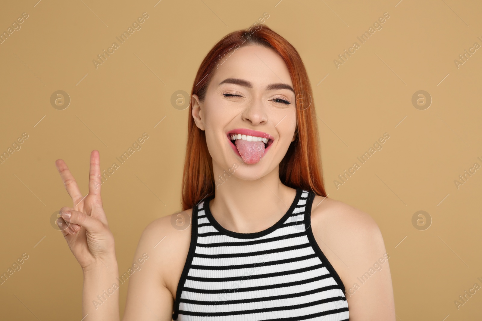 Photo of Happy woman showing her tongue and V-sign on beige background