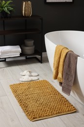 Photo of Stylish bathroom interior with bath tub, houseplant and soft yellow mat