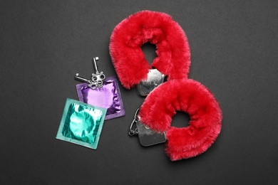 Photo of Furry handcuffs and condoms on black background, top view. Sex game