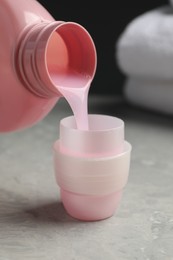 Pouring laundry detergent from bottle into cap on light grey marble table, closeup