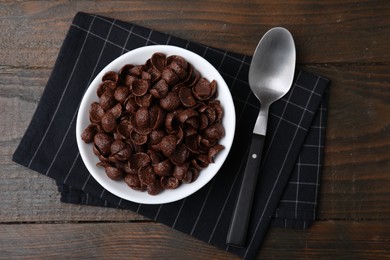 Photo of Chocolate corn flakes in bowl and spoon on wooden table, top view. Breakfast cereal