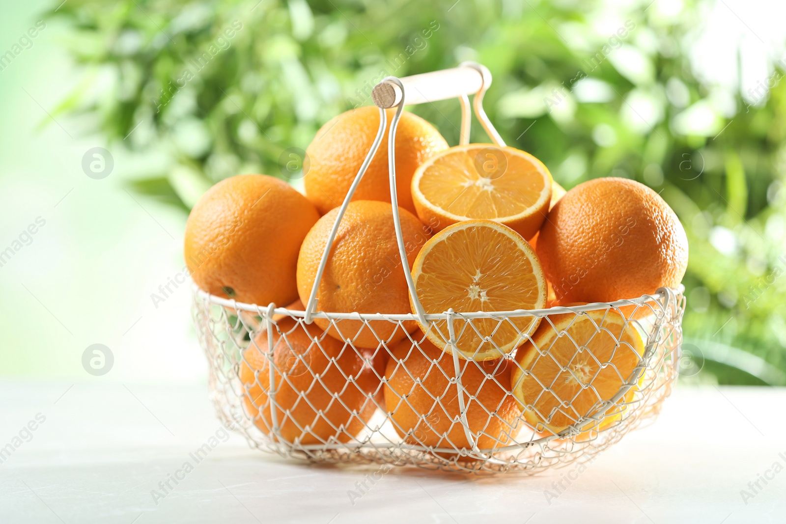 Photo of Basket with ripe oranges on table against blurred background