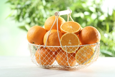 Photo of Basket with ripe oranges on table against blurred background