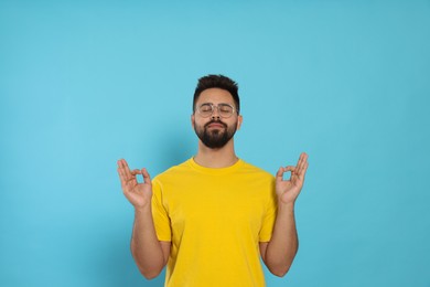 Photo of Young man meditating on light blue background. Zen concept