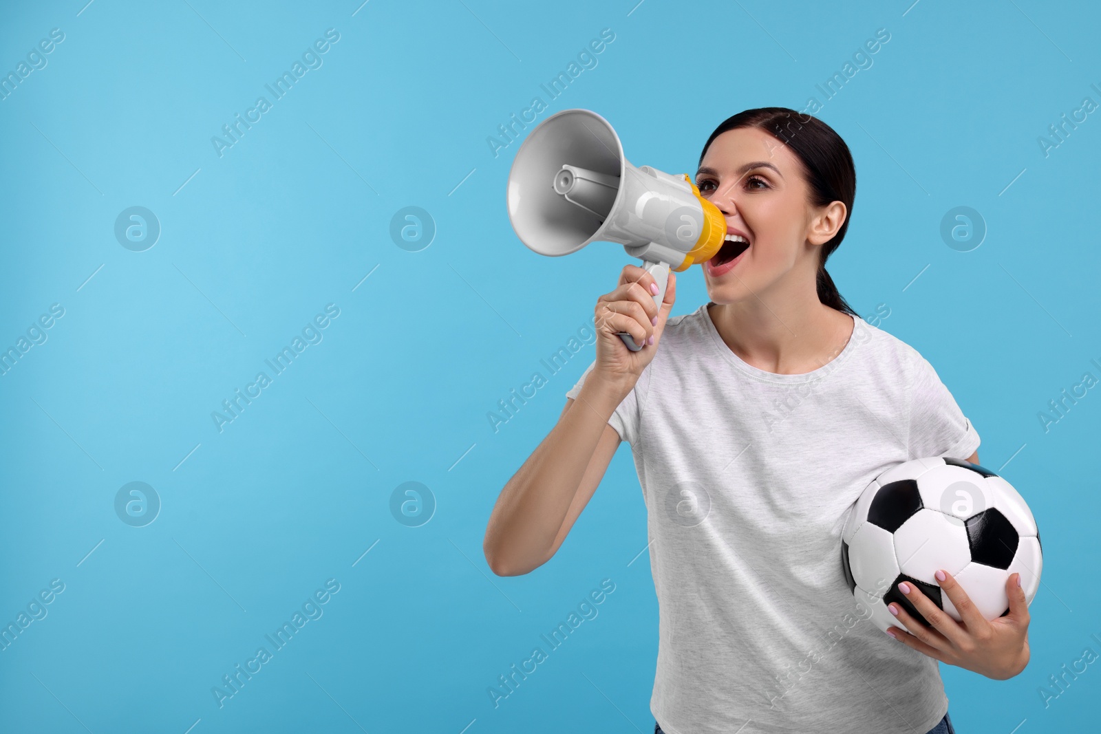 Photo of Emotional sports fan with soccer ball and megaphone on light blue background, space for text