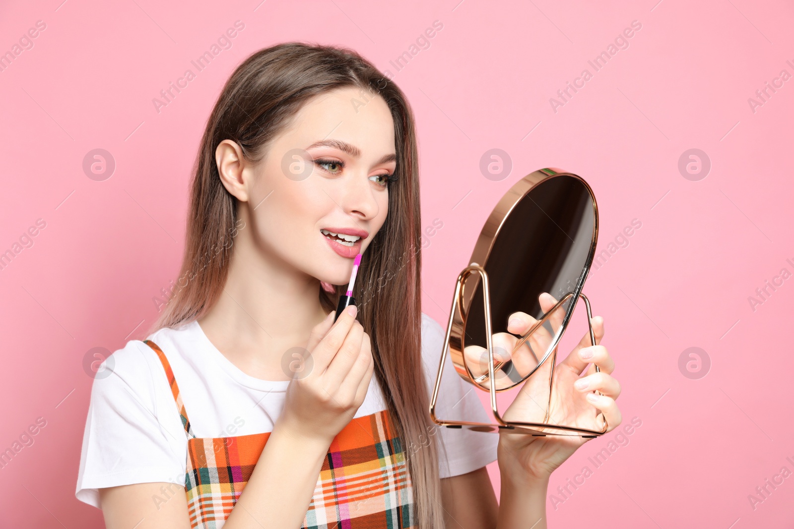 Photo of Beauty blogger applying lipgloss on pink background