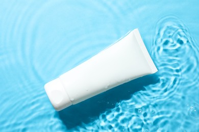 Photo of Tube with moisturizing cream in water on light blue background, top view