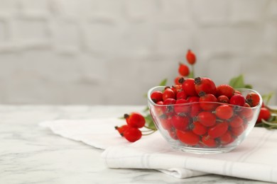 Photo of Ripe rose hip berries in bowl on white marble table. Space for text