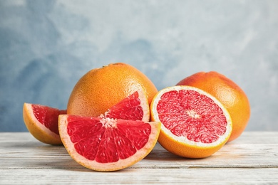 Photo of Composition with yummy grapefruits on wooden table against color background