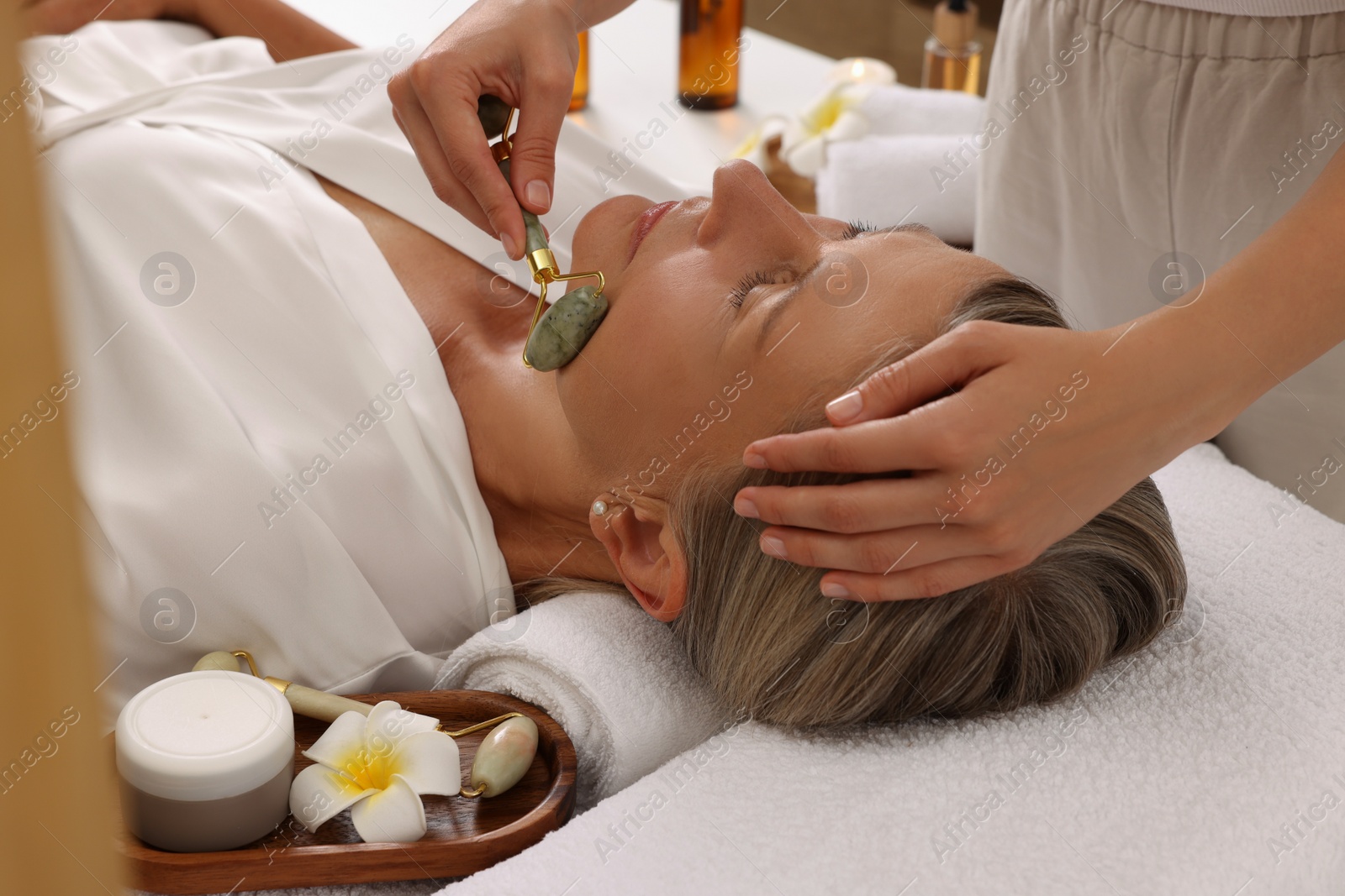 Photo of Woman receiving facial massage with jade roller in beauty salon, closeup