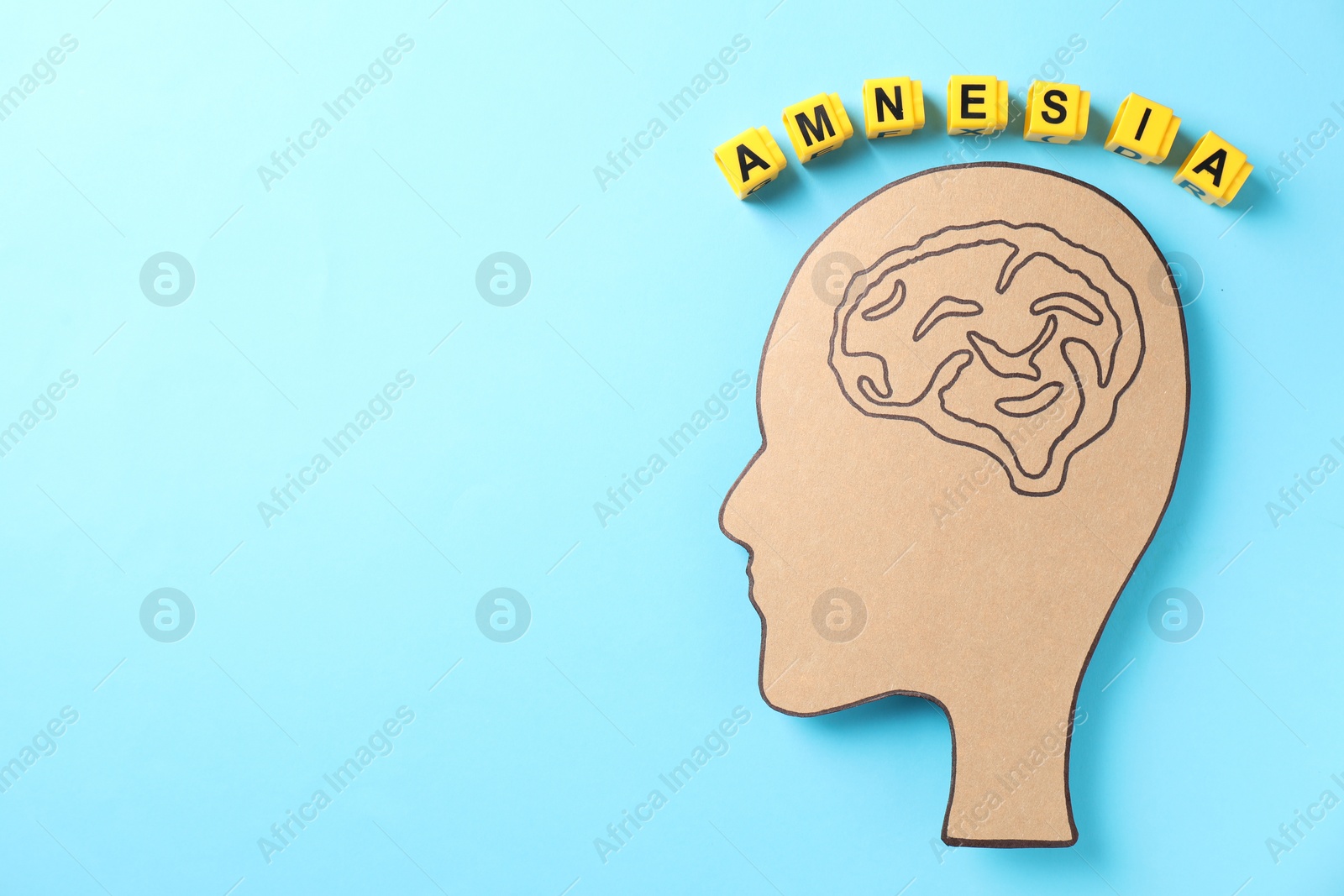 Photo of Yellow cubes with word Amnesia and human head cutout with drawing of brain on light blue background, top view. Space for text