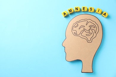 Yellow cubes with word Amnesia and human head cutout with drawing of brain on light blue background, top view. Space for text