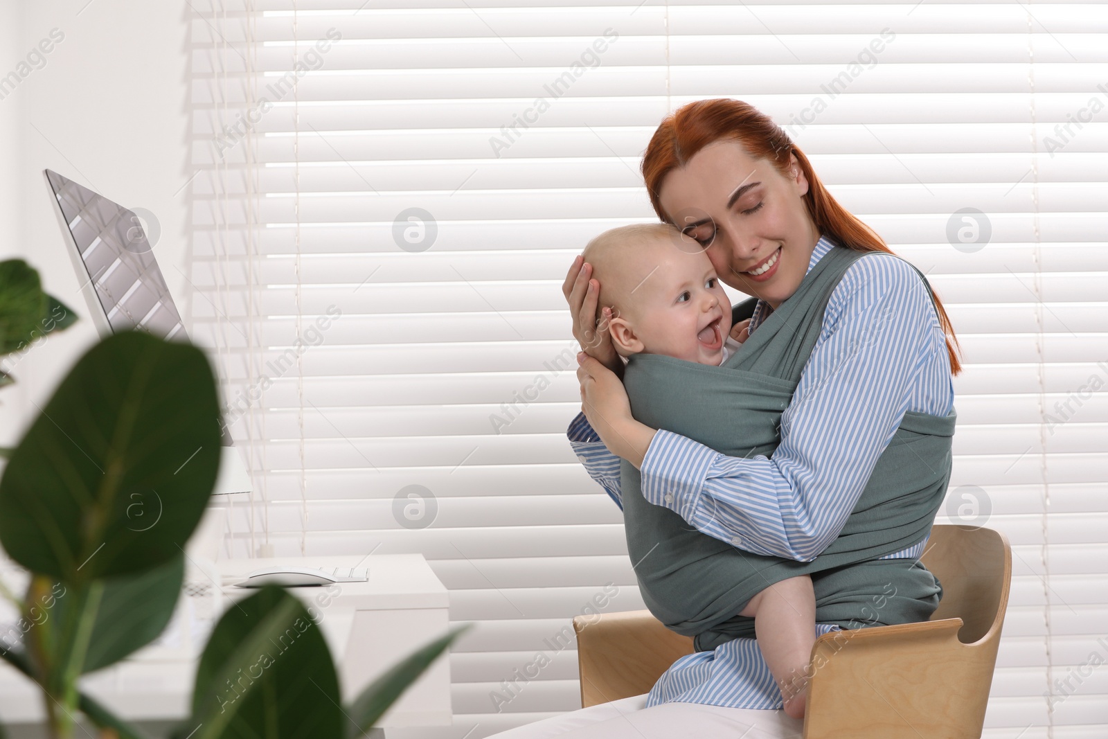 Photo of Mother holding her child in sling (baby carrier) at workplace