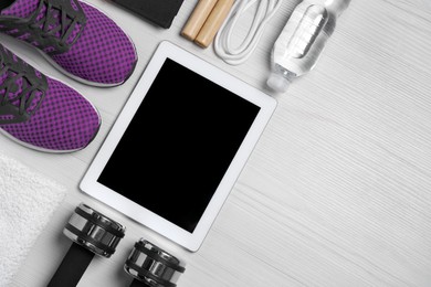 Photo of Tablet, sneakers and sports equipment on white wooden table, flat lay with space for text. Personal training