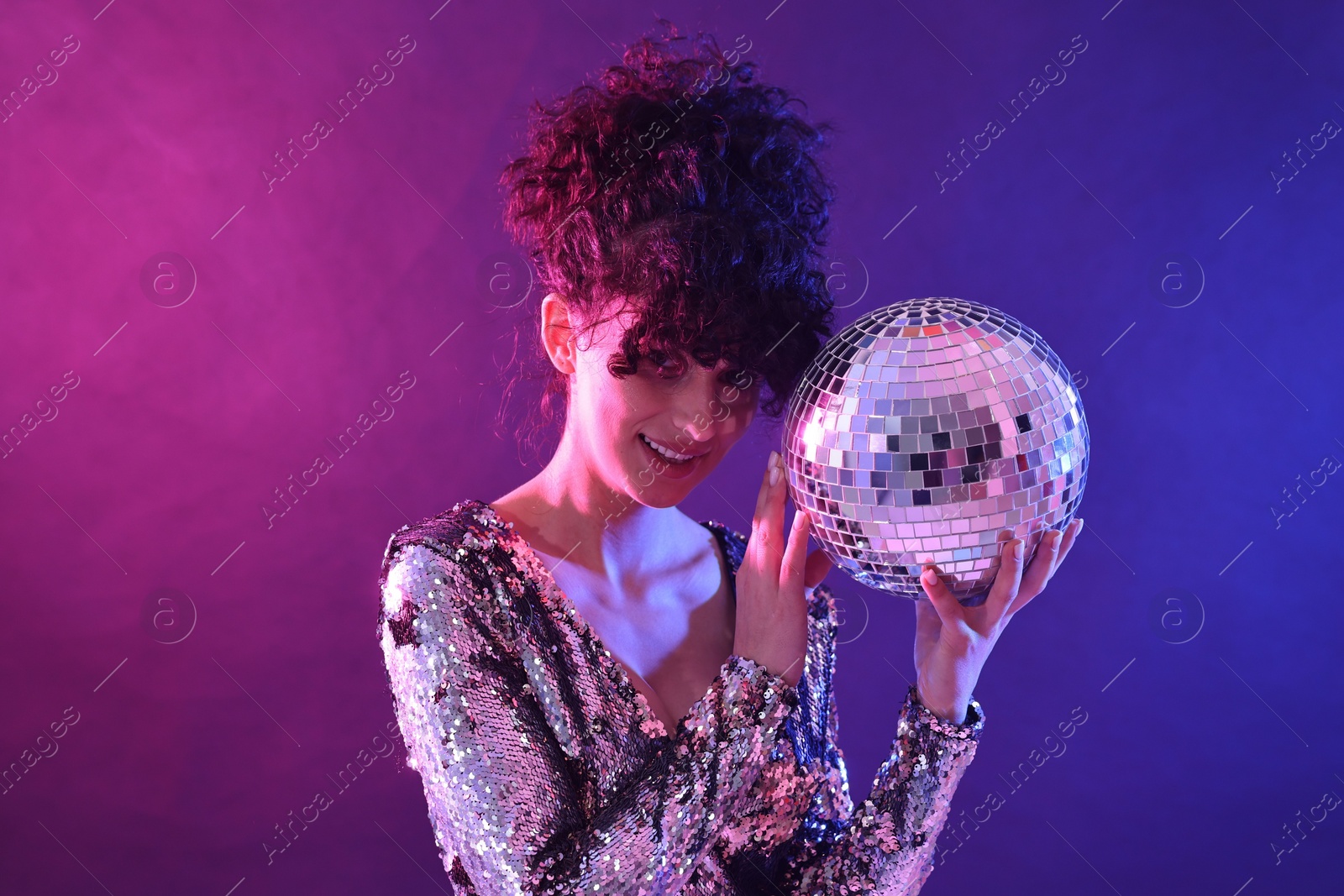 Photo of Beautiful young woman with disco ball posing on color background in neon lights