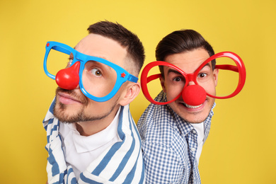 Photo of Men with funny accessories on yellow background. April fool's day
