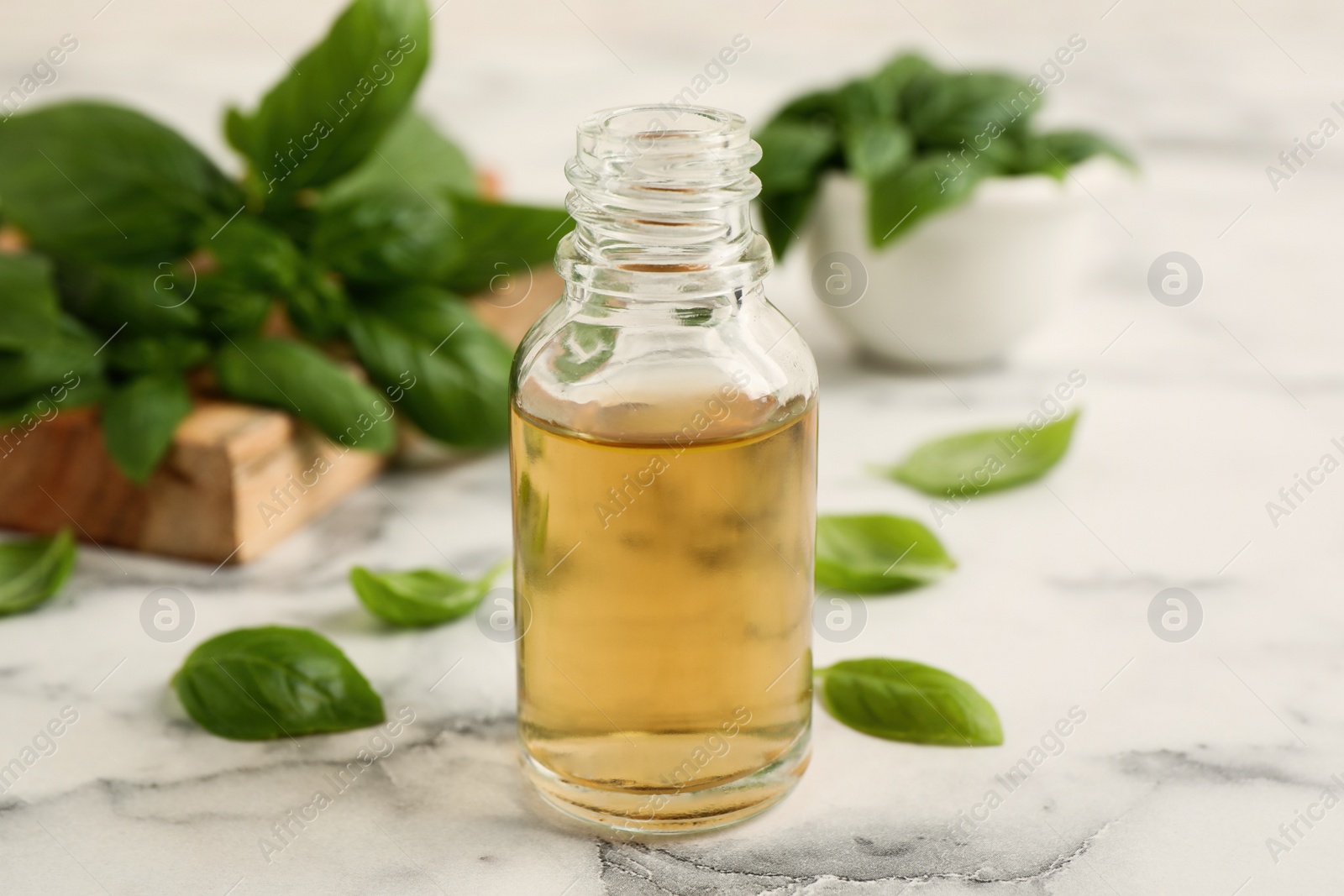 Photo of Glass bottle of basil essential oil and leaves on white  marble table