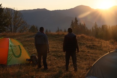Photo of Tourists enjoying sunrise near camping tents in mountains, back view