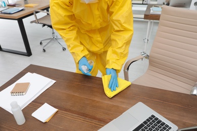 Photo of Janitor in protective suit disinfecting office furniture to prevent spreading of COVID-19, closeup