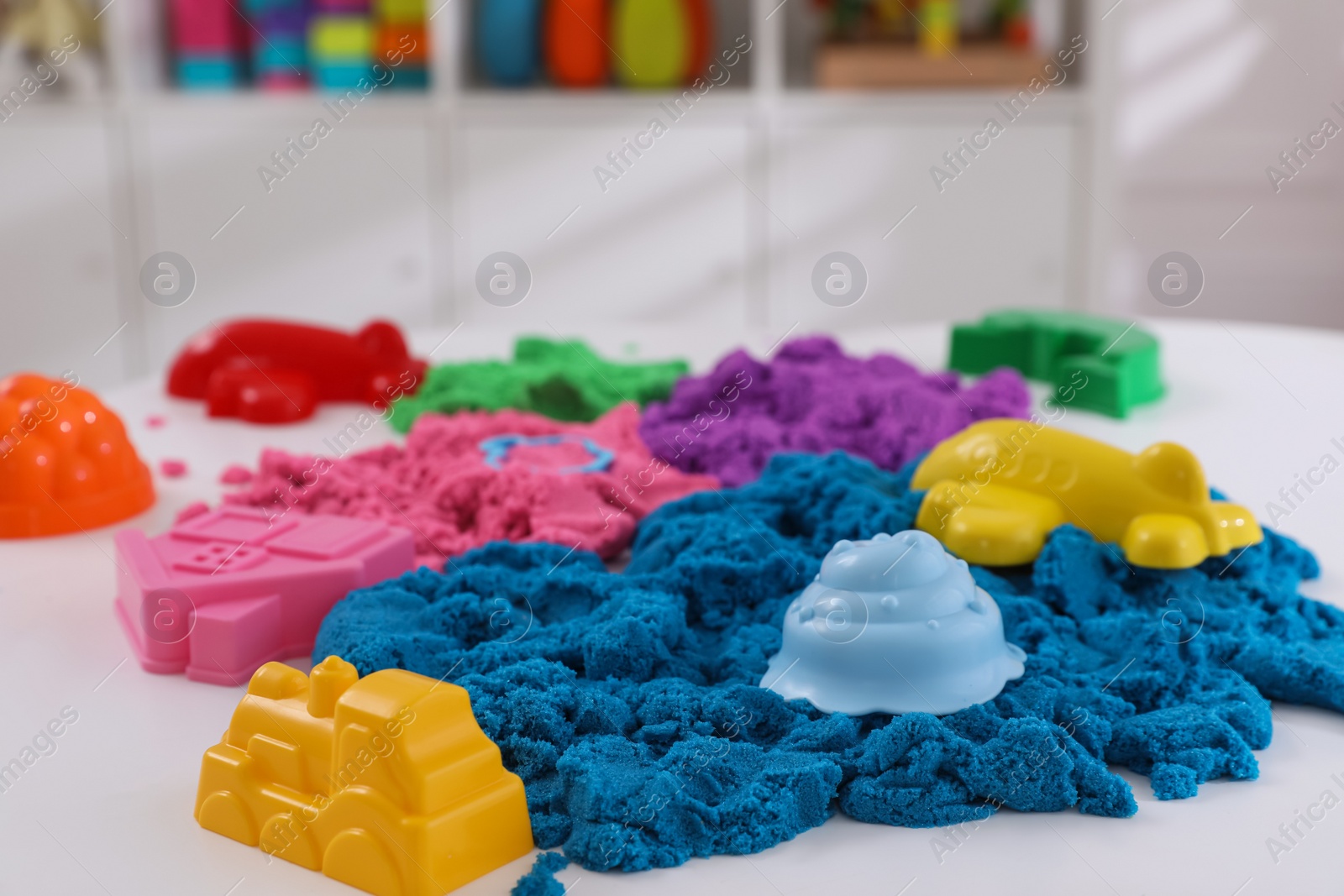 Photo of Bright kinetic sand and toys on white table indoors
