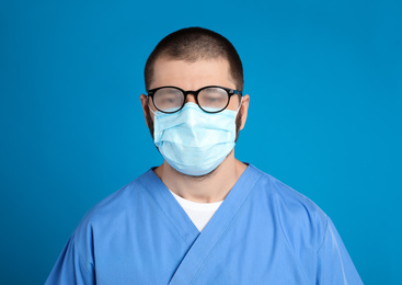 Photo of Doctor with foggy glasses caused by wearing disposable mask on blue background. Protective measure during coronavirus pandemic