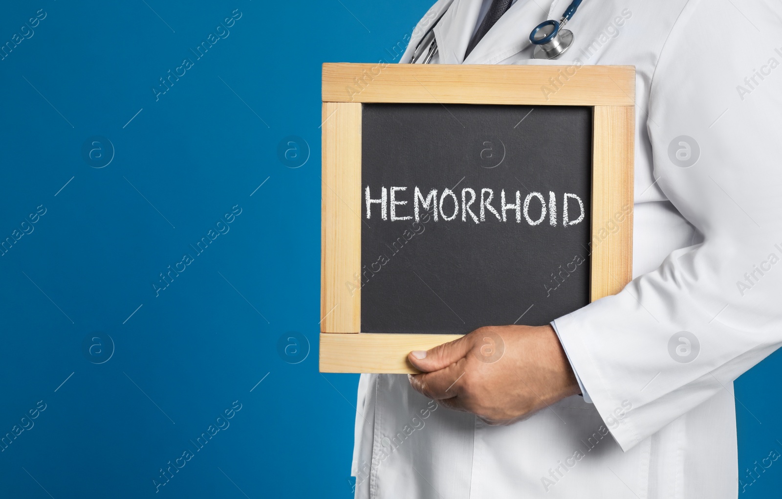 Photo of Doctor holding blackboard with word HEMORRHOID on blue background, closeup. Space for text