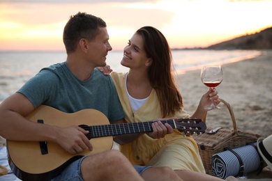 Lovely couple with guitar and picnic basket on beach at sunset