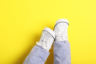 Photo of Little baby in stylish gumshoes on yellow background, top view