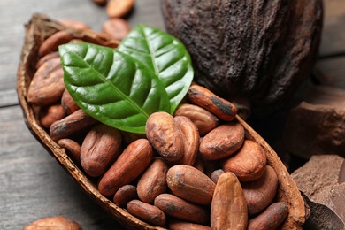Photo of Cocoa pod with beans and leaves on table, closeup