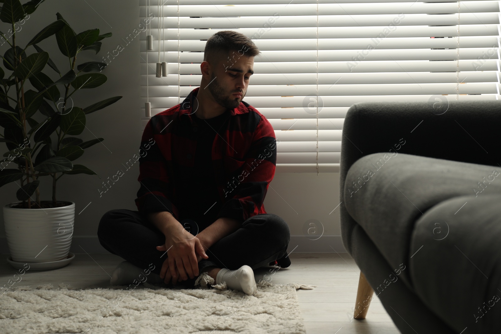 Photo of Sad man sitting near closed blinds indoors