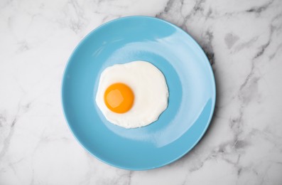 Tasty fried egg in plate on white marble table, top view