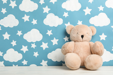 Teddy bear on white wooden table near wall with painted blue sky, space for text. Baby room interior