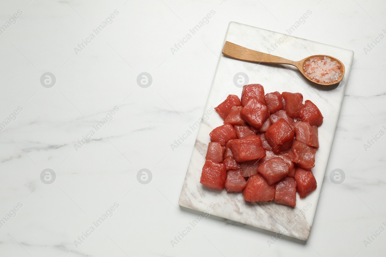 Photo of Cooking delicious goulash. Raw beef meat and sea salt on white marble table, top view. Space for text
