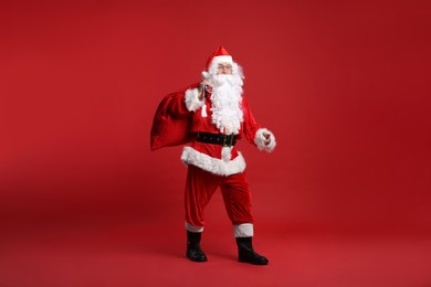 Santa Claus with bag of Christmas presents posing on red background