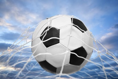 Soccer ball in net against cloudy sky