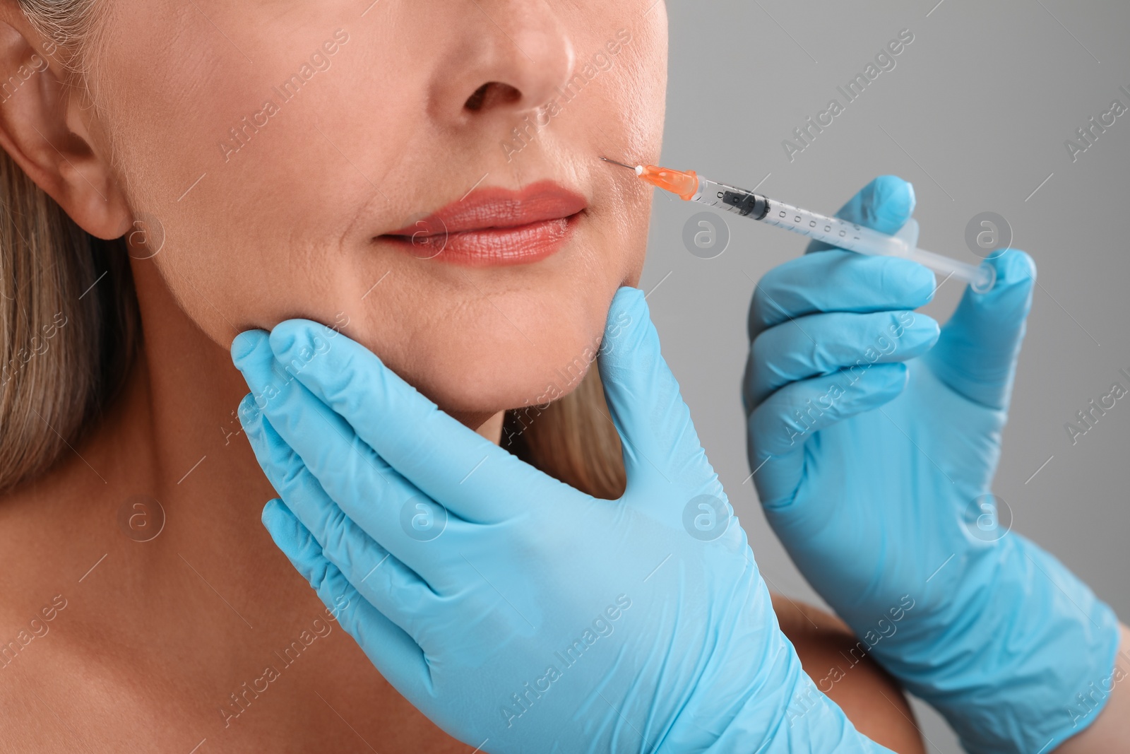 Photo of Doctor giving facial injection to senior woman on light grey background, closeup. Cosmetic surgery